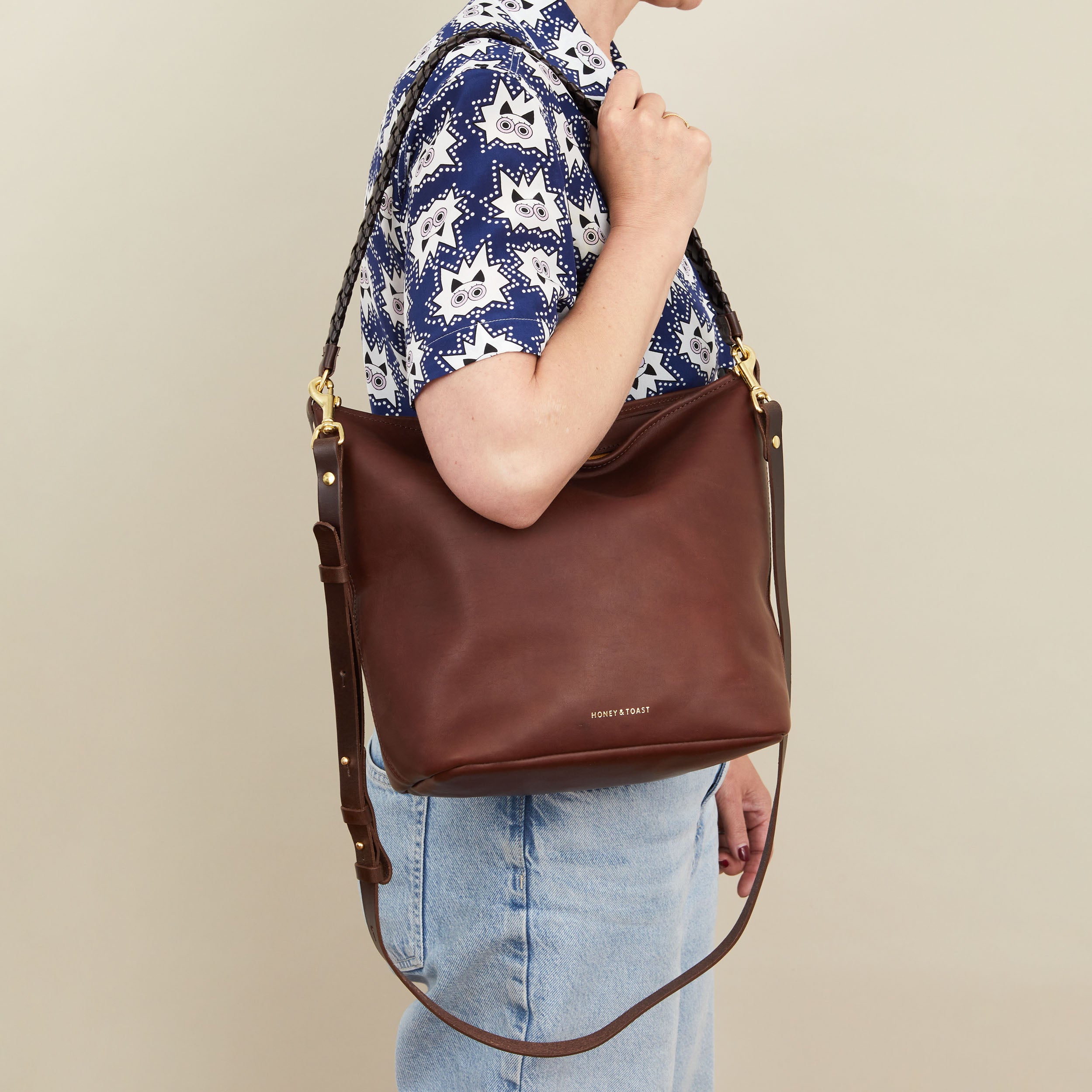 Person holding a brown leather handbag with a neutral background